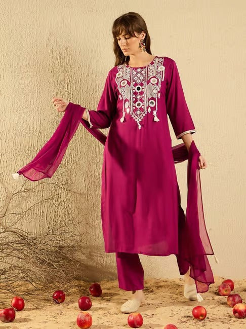 Woman wearing a magenta embroidered outfit with a plain background